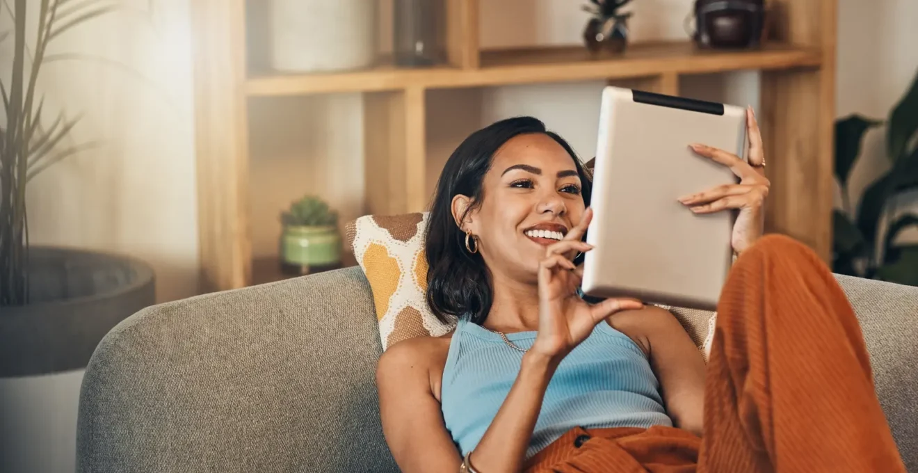 Une personne compare différentes offres bancaires sur une tablette tout en prenant des notes manuscrites dans son salon